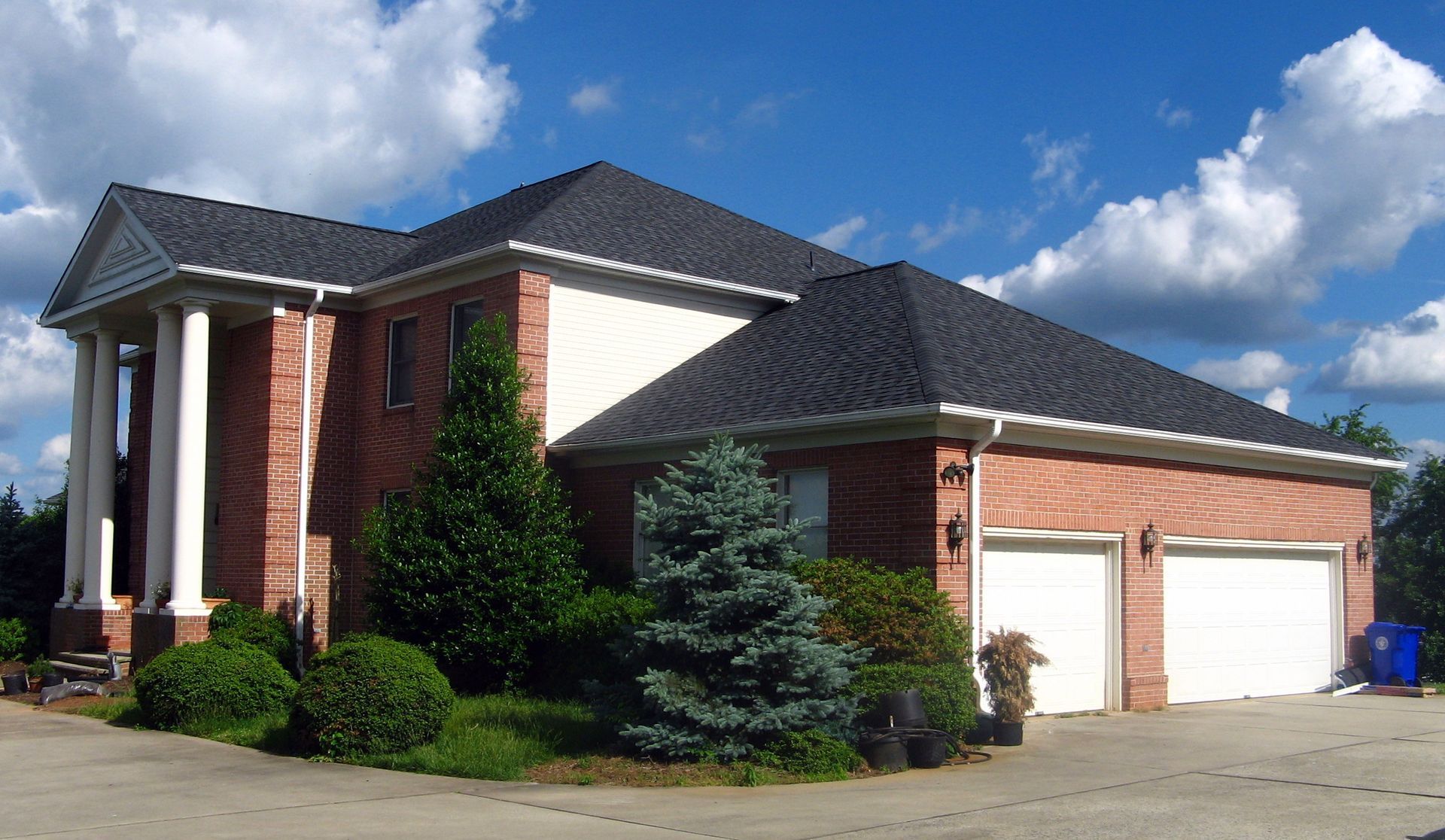 A large brick house with a black roof and white garage doors