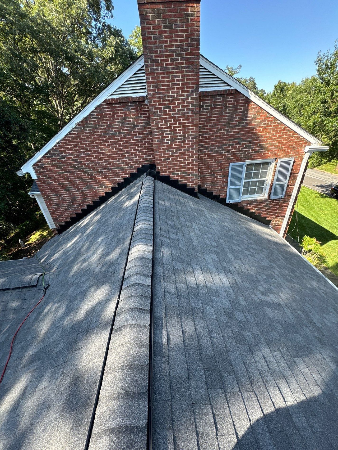 Roof of a house with asphalt shingles, brick chimney, and triangular roof above.
