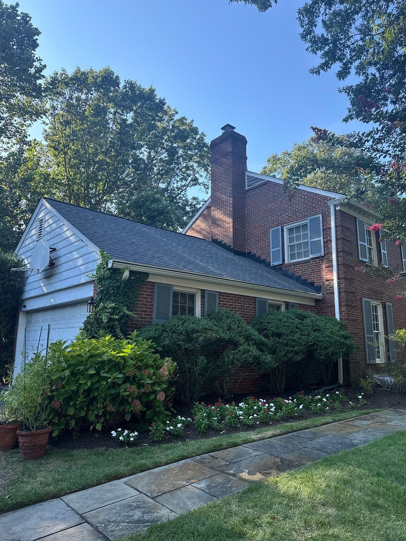 Brick house with attached garage, blue shutters, green lawn, and trees.