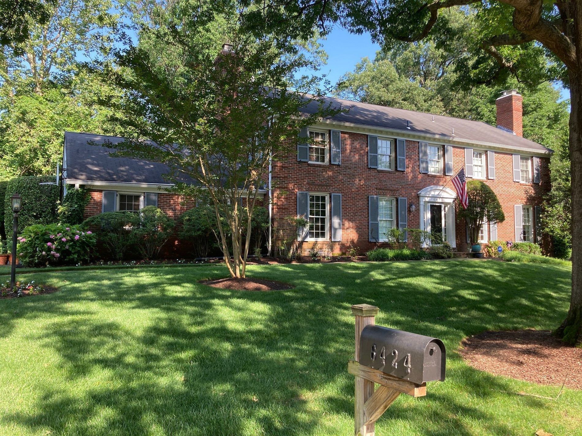 Red brick house with blue shutters, mailbox in front on a sunny day.