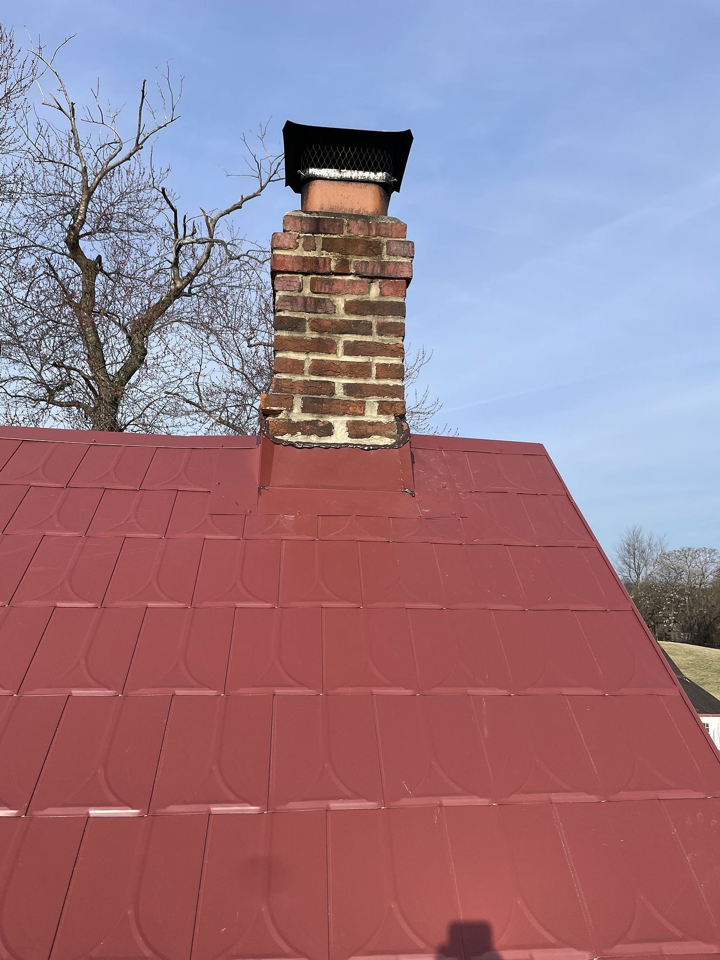 Red metal roof with a brick chimney and a black cap.