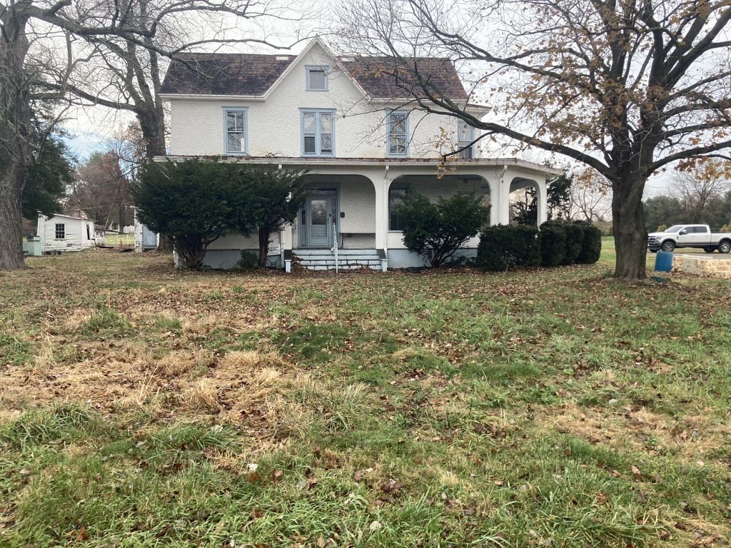 Two-story white house with a porch, bushes, and a patchy lawn under a cloudy sky.