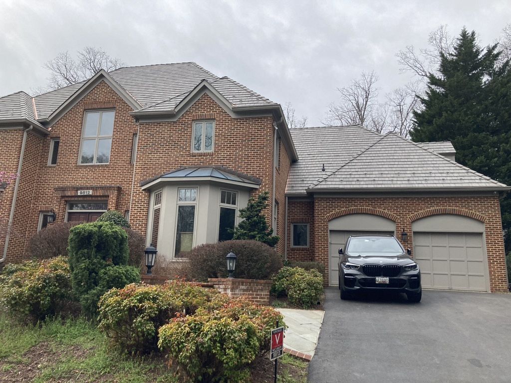 Two-story brick house with a black SUV in the driveway. Overcast day. Beige garage doors.