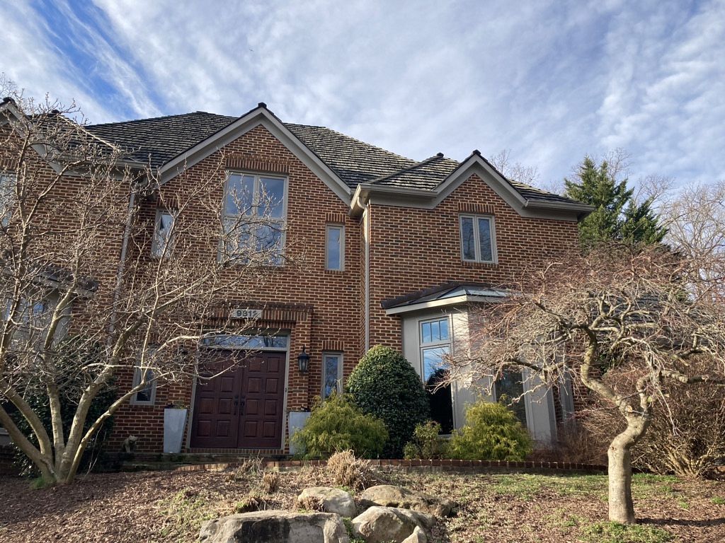 Two-story brick house with brown door and leafless trees under a blue sky.