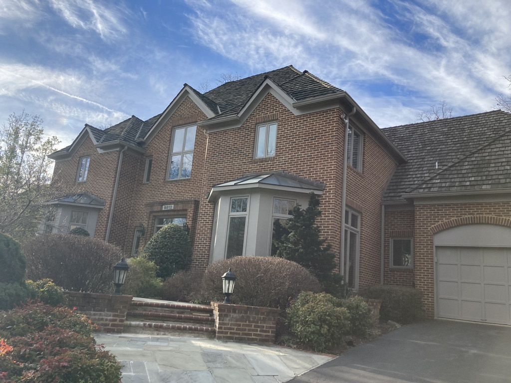 Brick house with multiple stories, arched windows, and driveway on a sunny day.