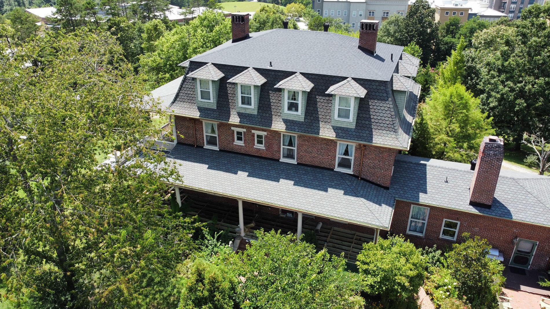 An aerial view of a brick house with a Mansard roof, surrounded by trees.