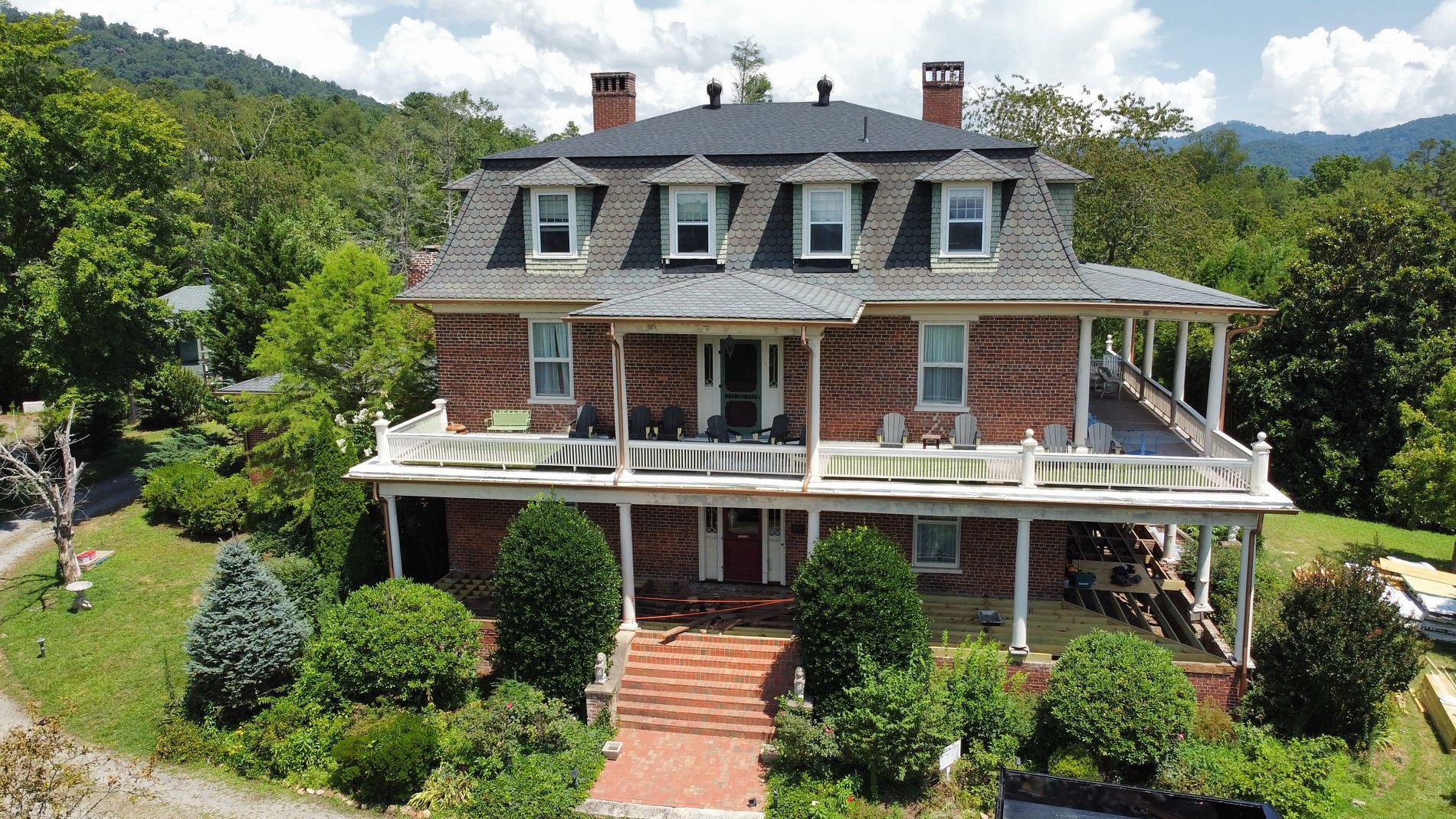 Brick mansion with a wrap-around porch, set against a backdrop of trees and mountains.