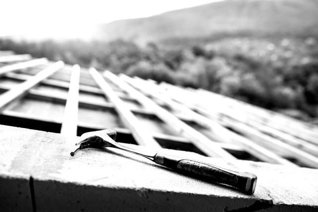 A black and white photo of a hammer and nails on a roof.