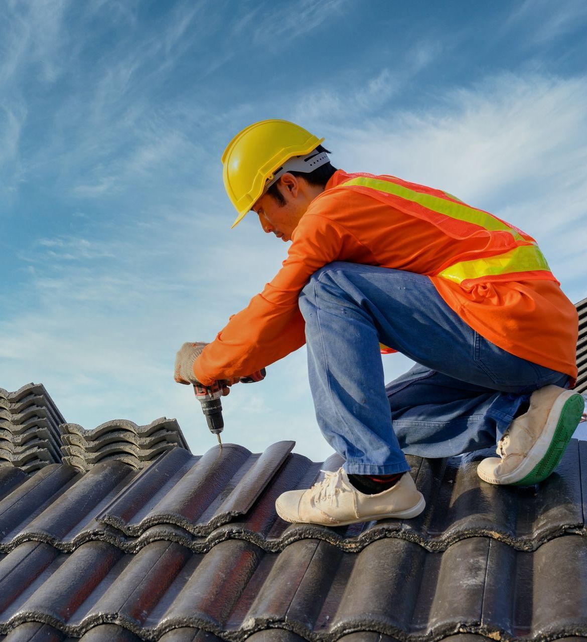A man is kneeling on a roof using a drill