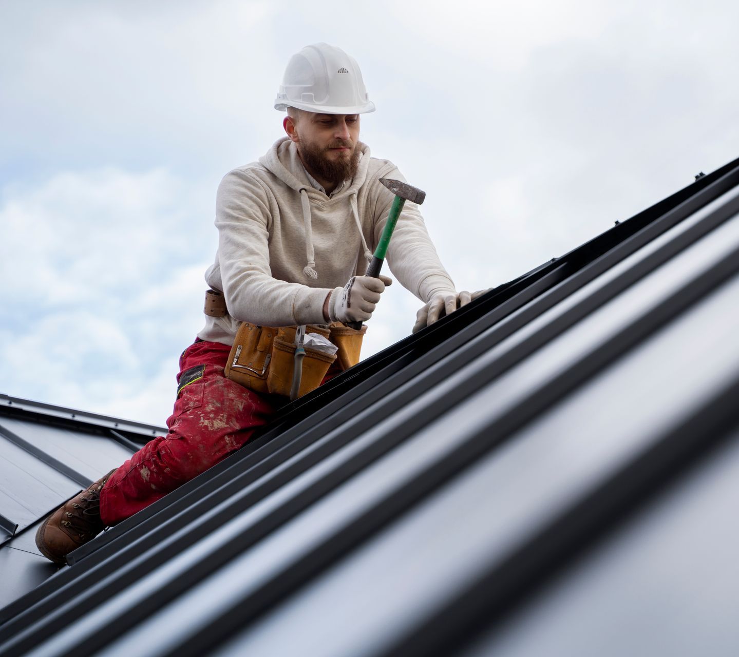 A man is sitting on top of a roof holding a hammer.