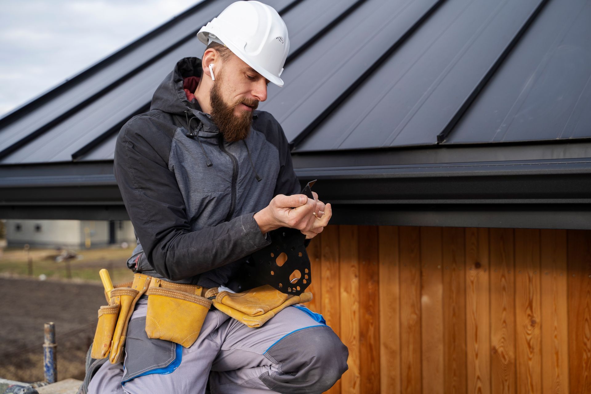 A construction worker is sitting on the roof of a building looking at his phone.