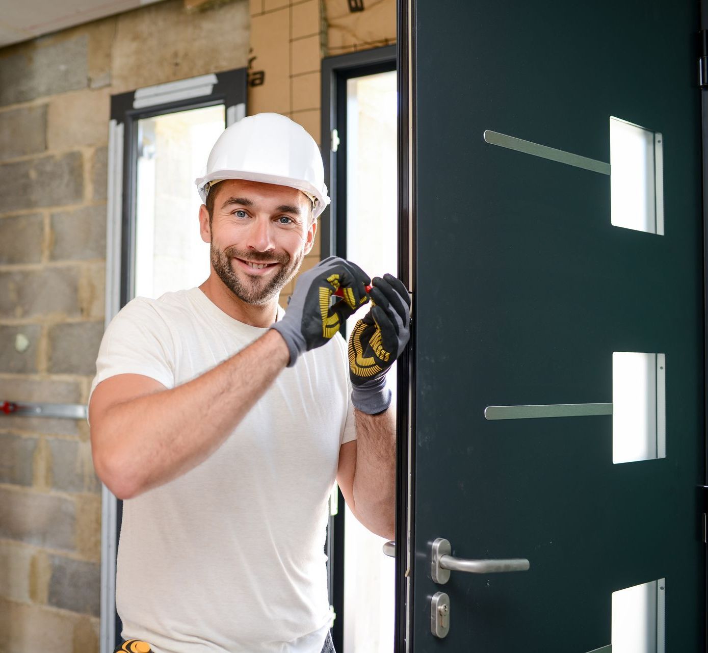 A man wearing a hard hat and gloves is standing in front of a door.