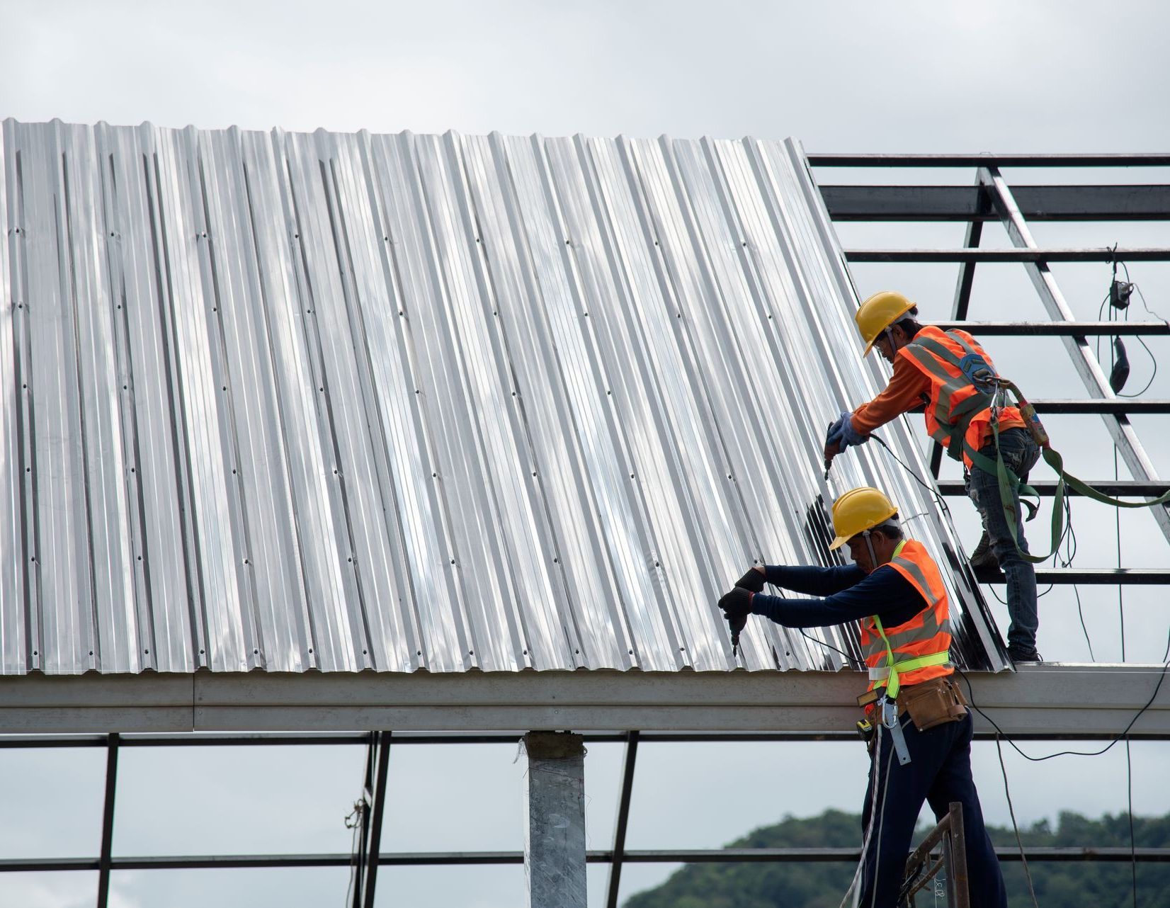 Two construction workers are working on a metal roof.