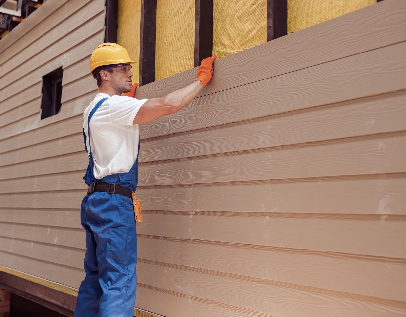 A man is installing siding on the side of a house.