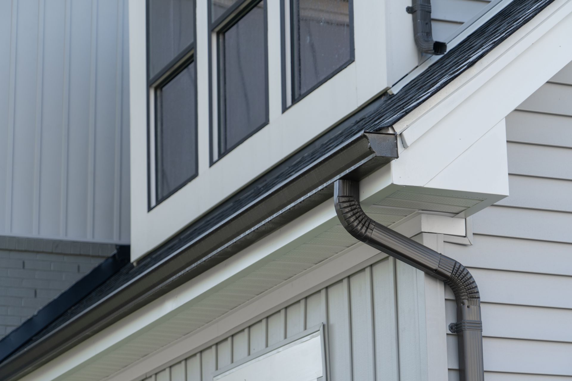 A man is standing on a ladder fixing a gutter on a house.