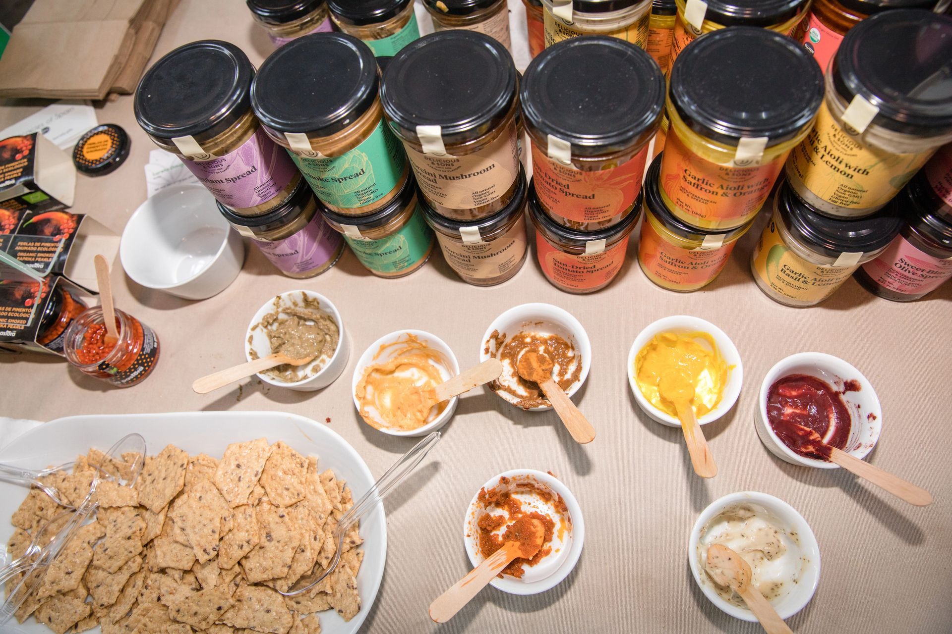 Tarros de conservas y pequeños cuencos con muestras, galletas y cucharas sobre una mesa.