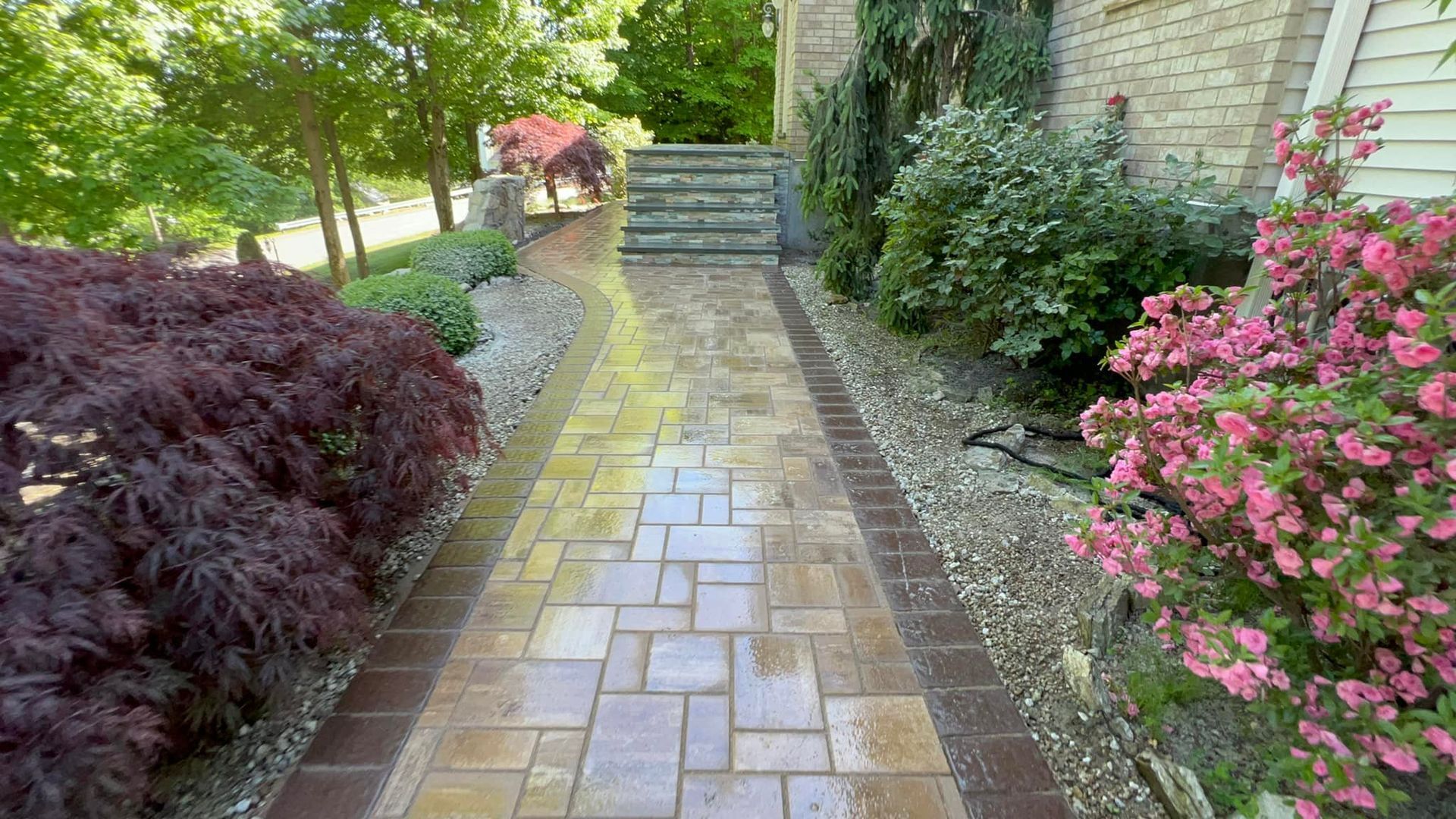 A brick walkway leading to a house surrounded by flowers and trees.