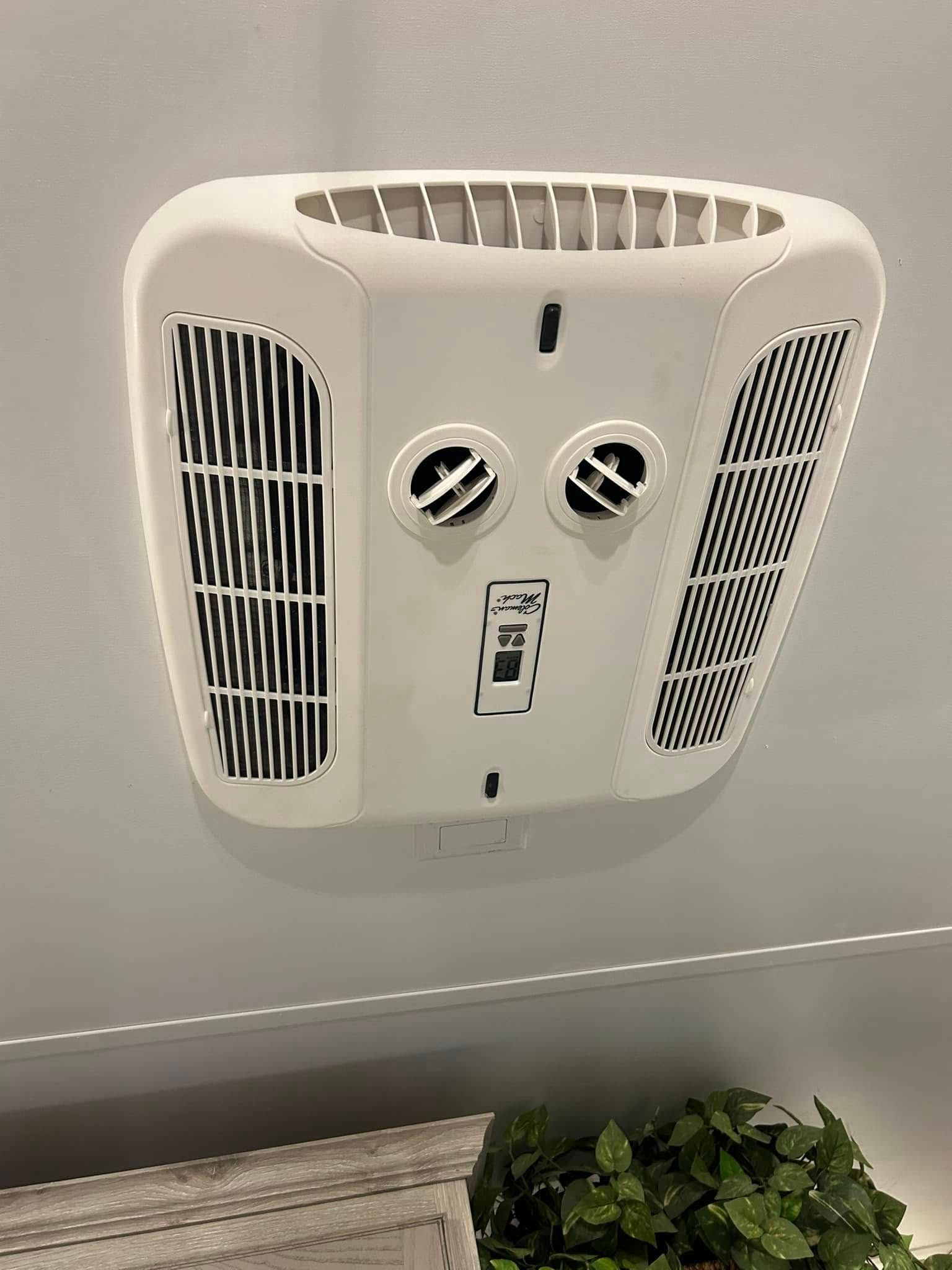 A white air conditioner is hanging on a wall next to a plant.
