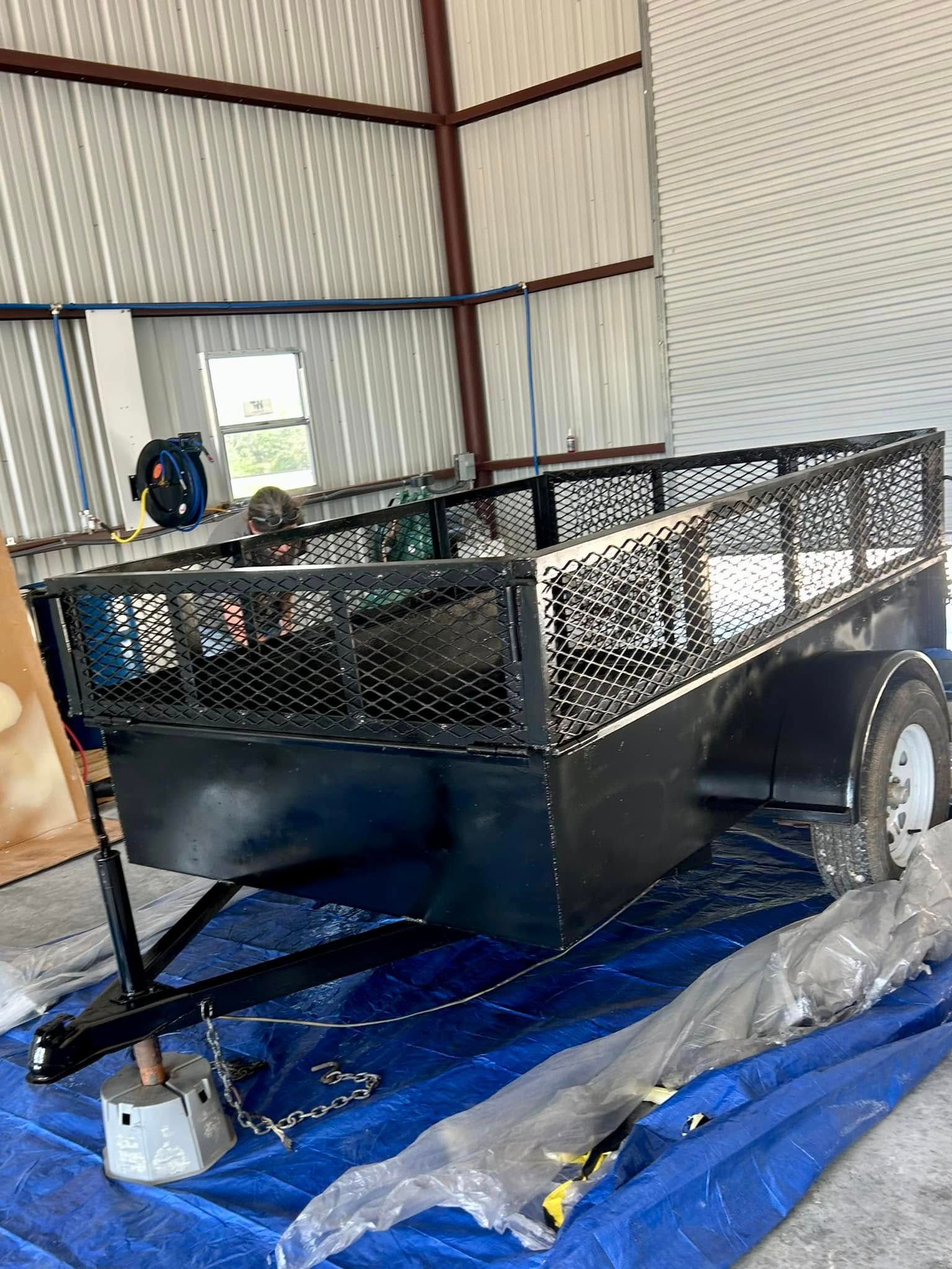 A black trailer is sitting on top of a blue tarp in a garage.