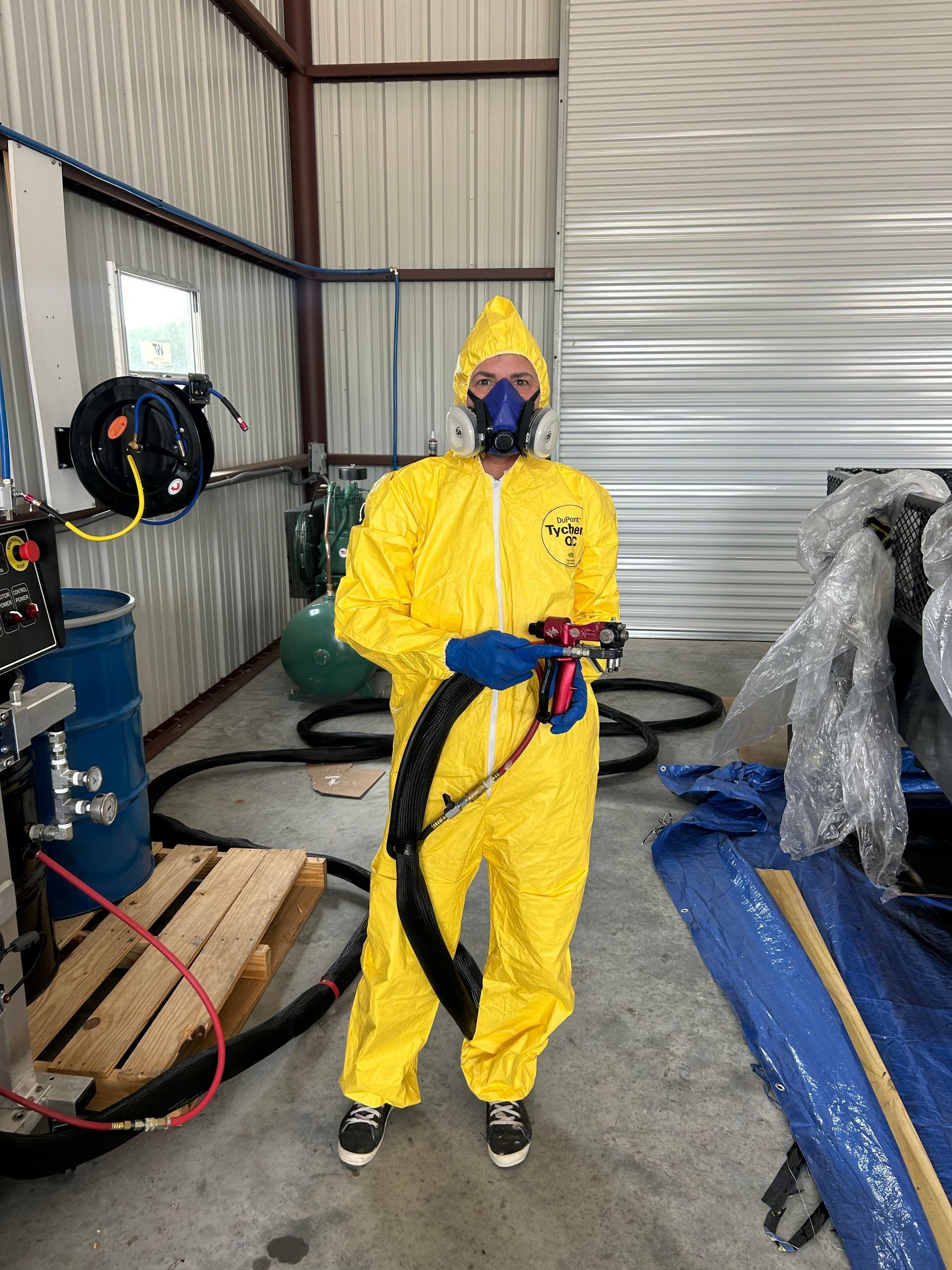 A man in a yellow protective suit is standing in a room holding a hose.