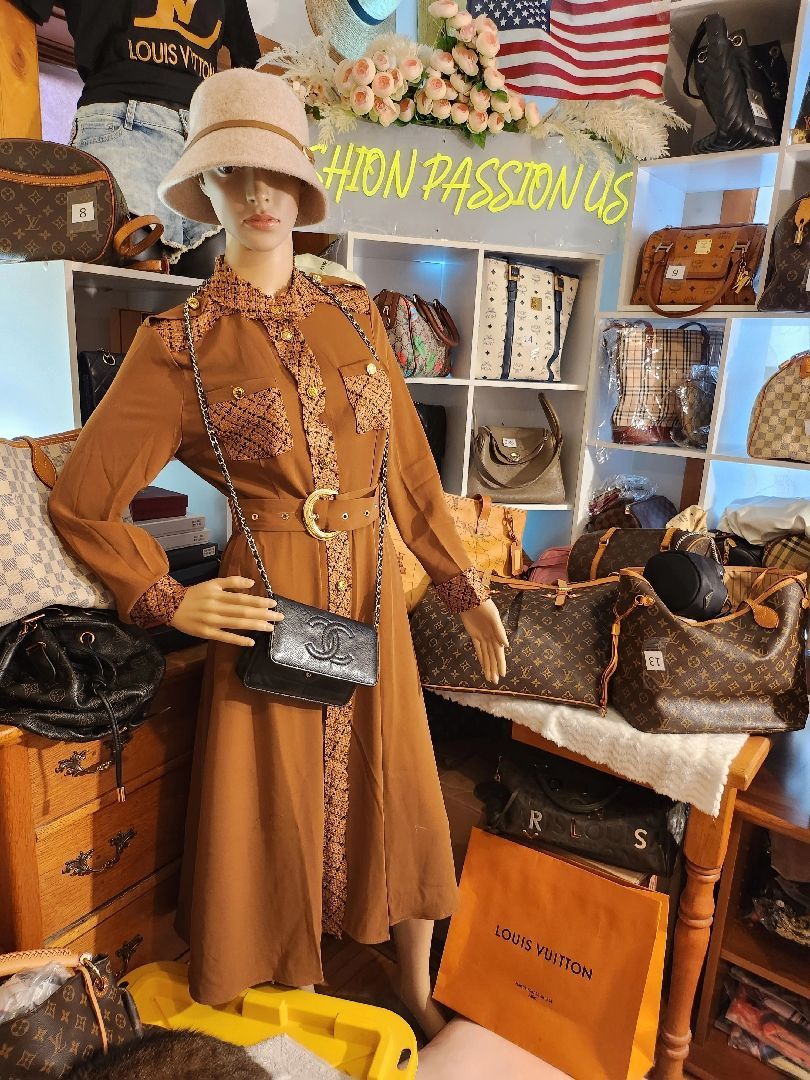 A mannequin wearing a brown dress and a hat is standing in front of a display of handbags.