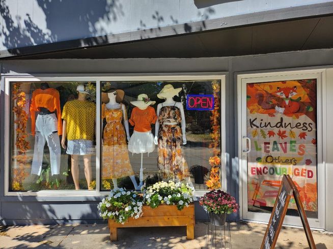 A store front with a window display of clothes and flowers.