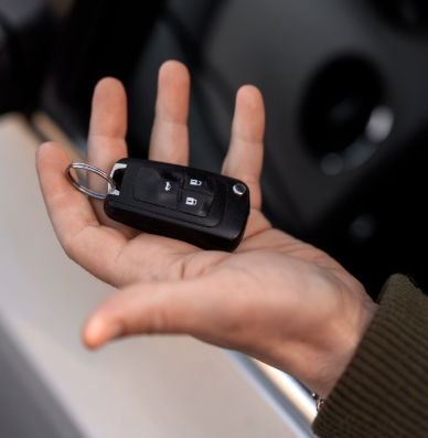Mano sosteniendo una llave de coche negra con botones remotos, cerca de un coche.