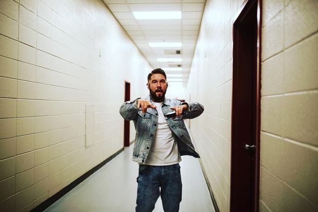 Man in denim jacket and jeans points toward the camera in a school hallway.