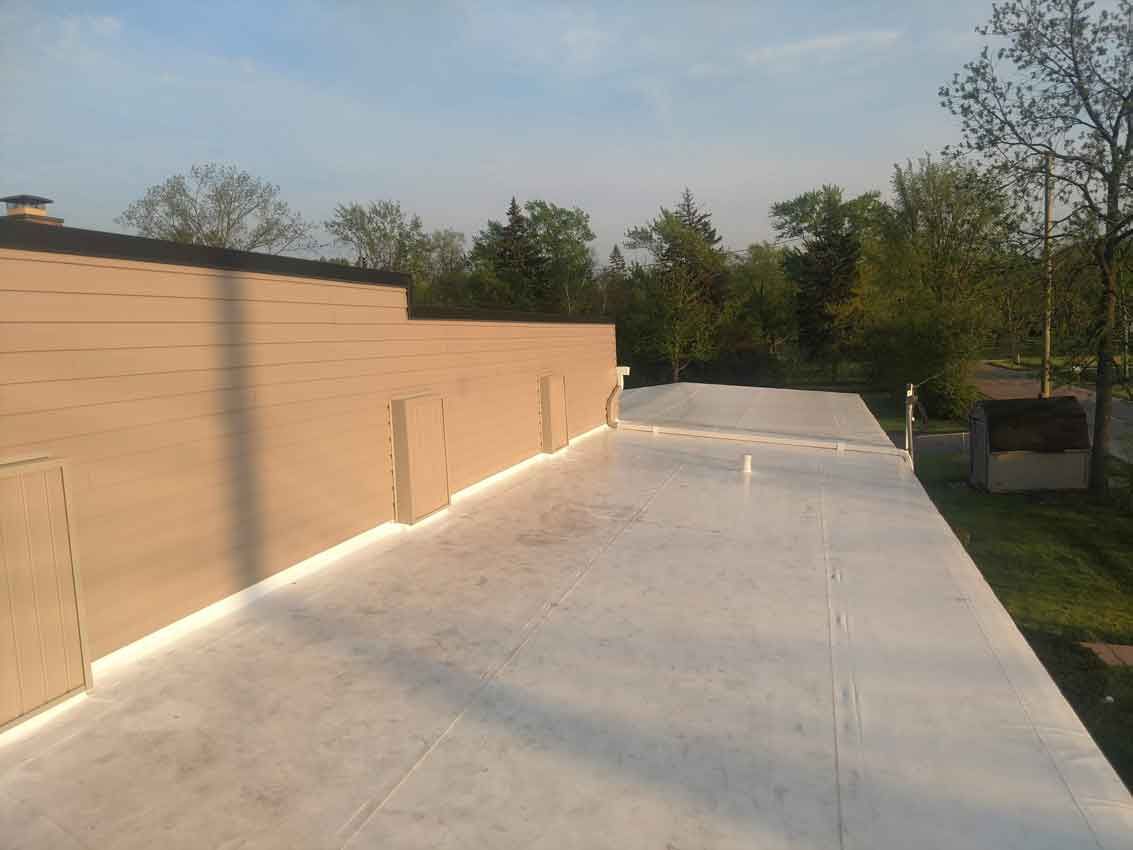 A white roof with a brick wall and trees in the background.