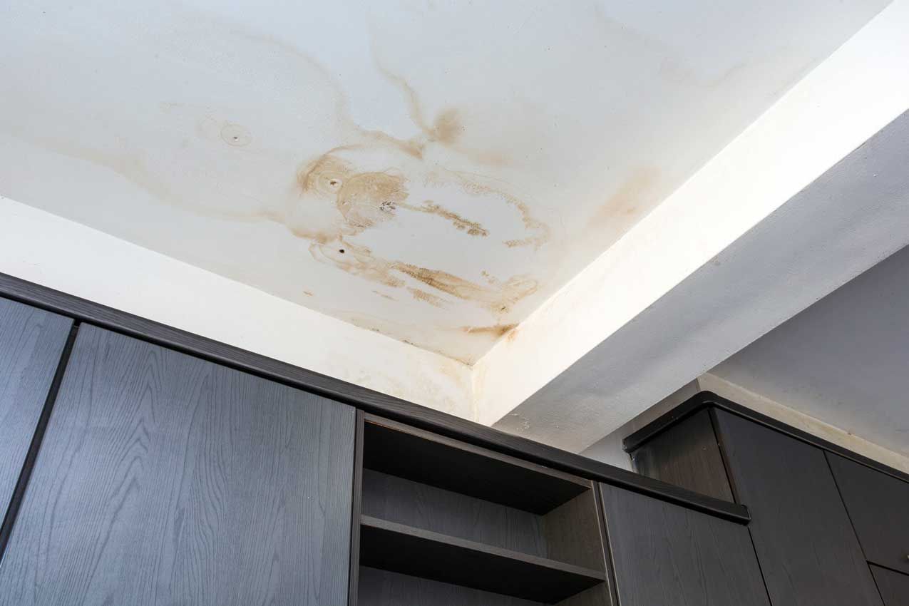 A ceiling with water stains on it in a room with cabinets.