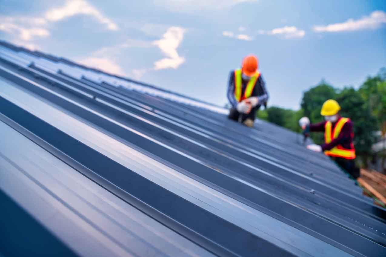 Two construction workers are working on a metal roof.