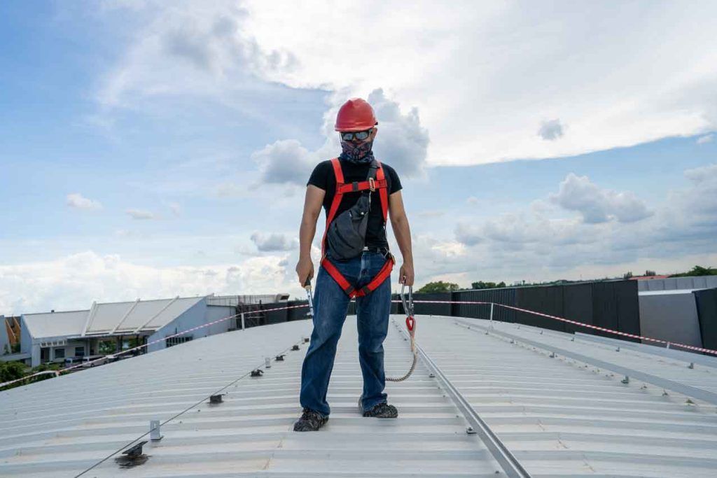 A man wearing a hard hat and safety harness is standing on a roof.