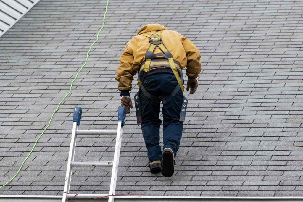 A man is walking up a ladder on a roof.