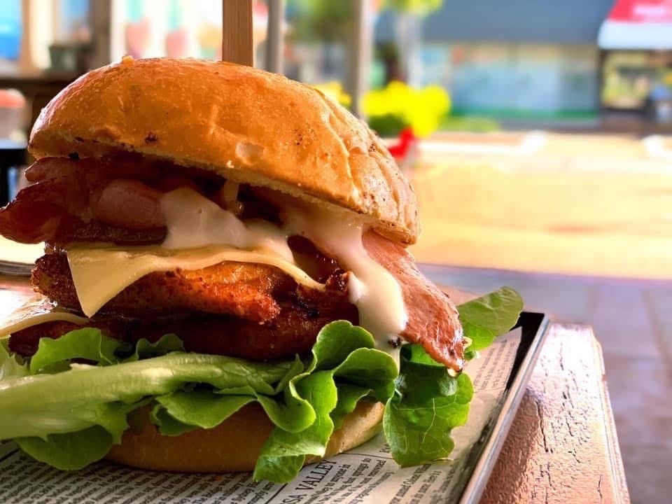 Burger with bacon, cheese, lettuce, and sauce, on a bun, placed on a newspaper-lined tray. — Cafe Nosh in Taree, NSW