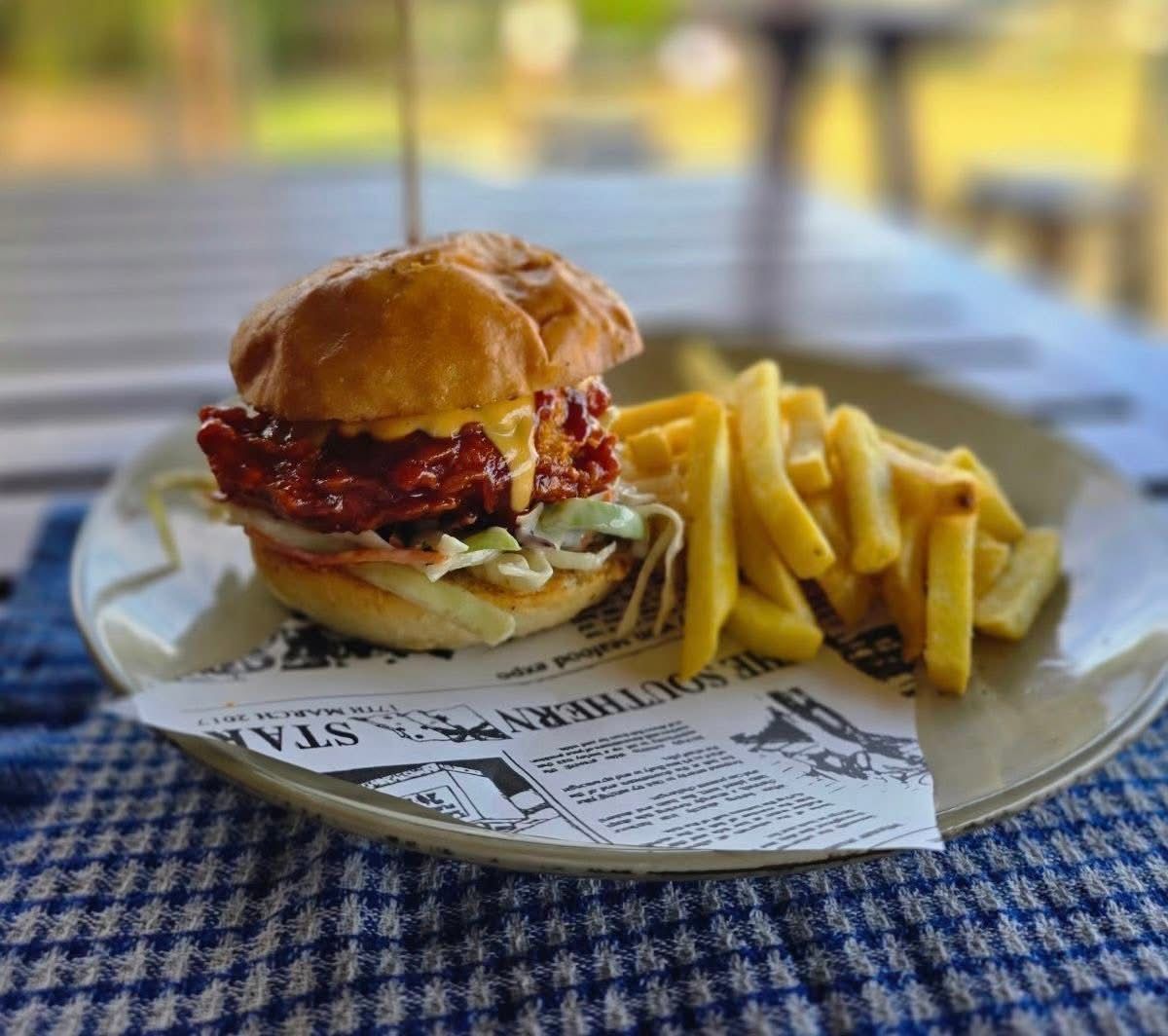 Burger with fries on a plate. The burger has a bun, patty, and toppings. Fries are golden. — Cafe Nosh in Taree, NSW