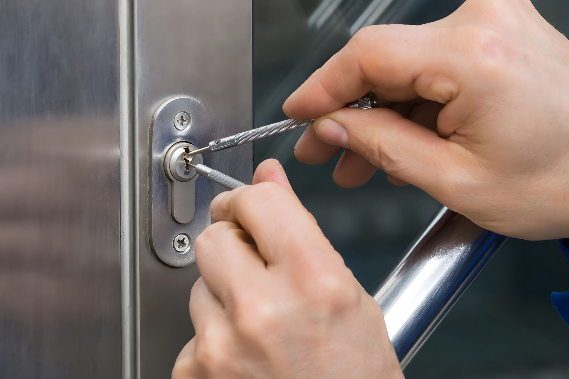 Hands picking a lock on a stainless steel door, using two metal tools