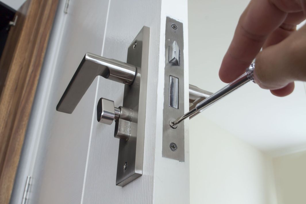 A person installing a silver door handle with a screwdriver on a white door