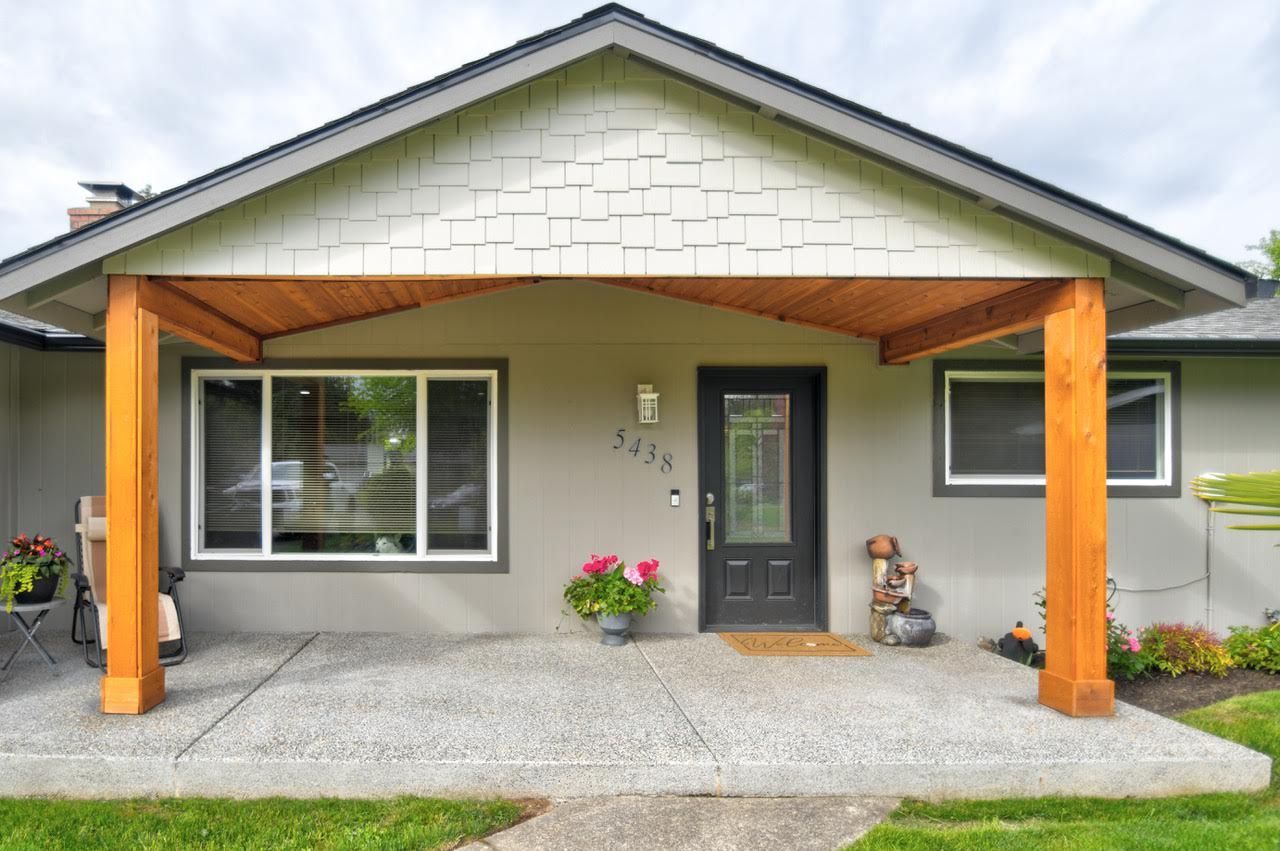 Tan house exterior with wood porch posts, a gray roof, and a black front door.