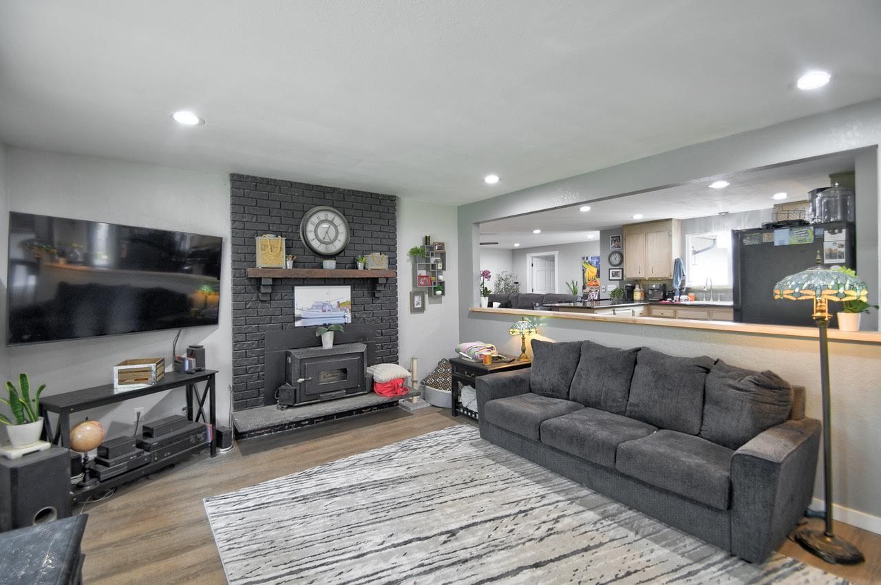 Living room with gray sofa, TV, black fireplace, and open kitchen view.