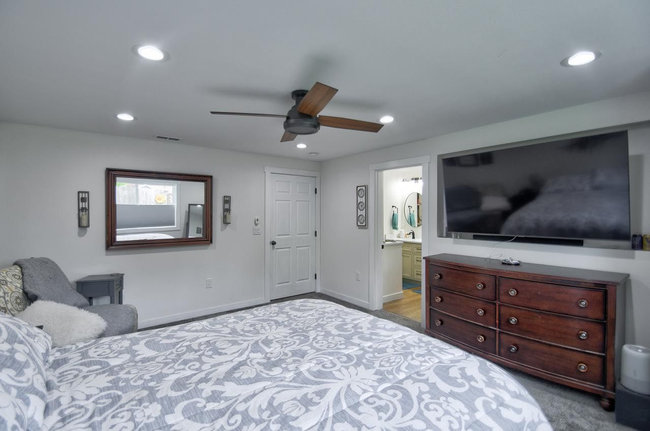 Bedroom with large TV above dresser, bed, mirror, door to bathroom.