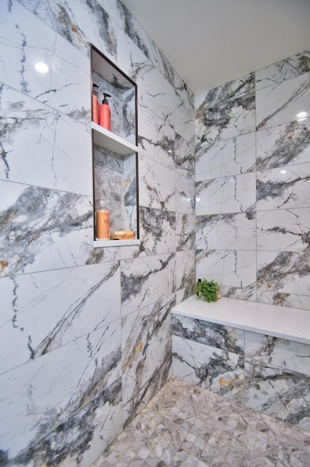 Luxurious marble-tiled shower with a built-in shelf holding toiletries; bench seat, pebble floor.