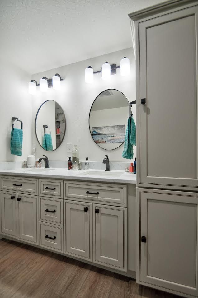 Bathroom with dual sinks, round mirrors, gray cabinets, white countertop, and turquoise towels.