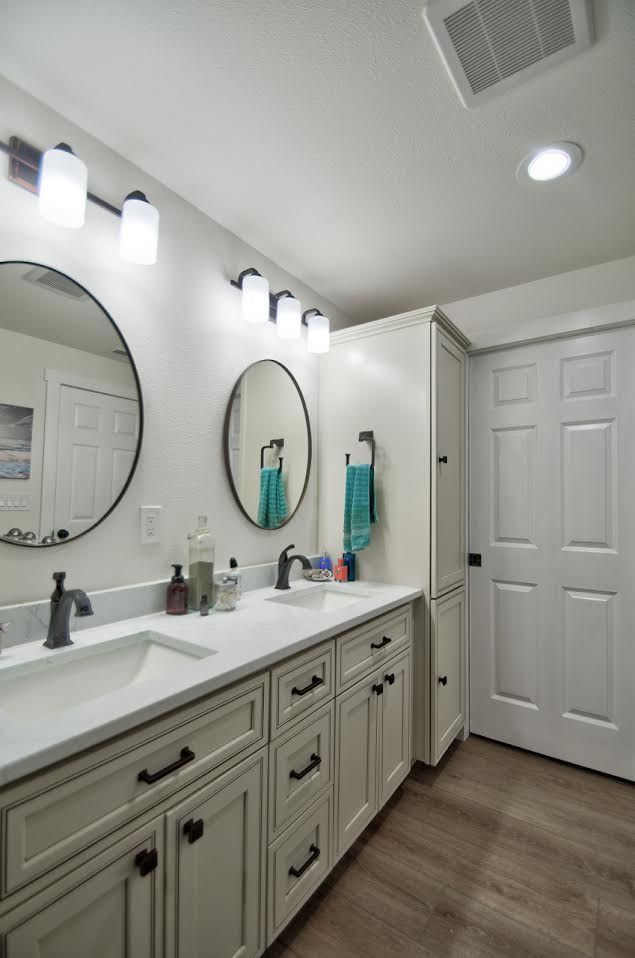 Bathroom with double vanity, round mirrors, and white cabinets.