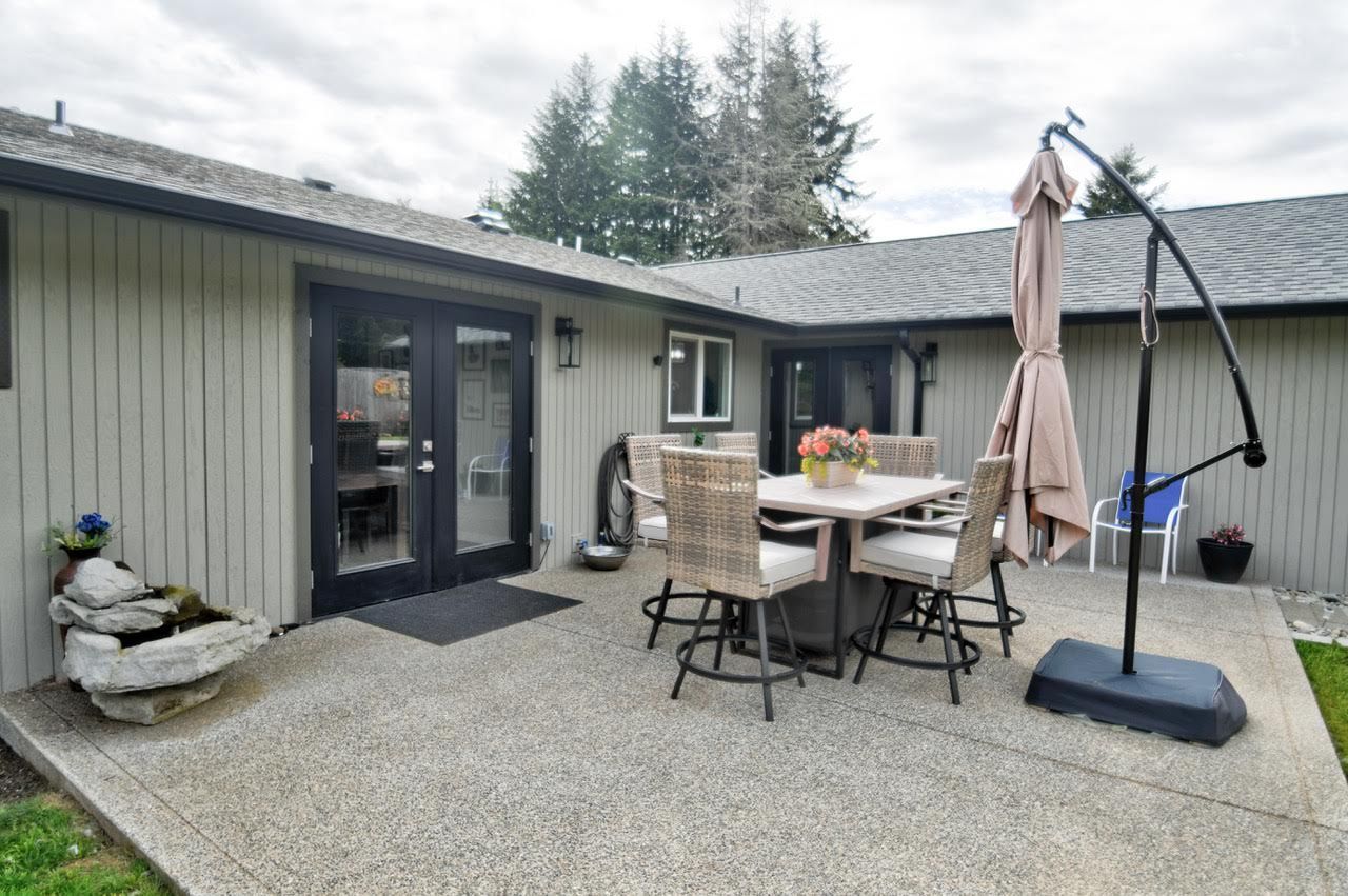 Patio with a table, chairs, and umbrella outside a house with French doors and a water feature.
