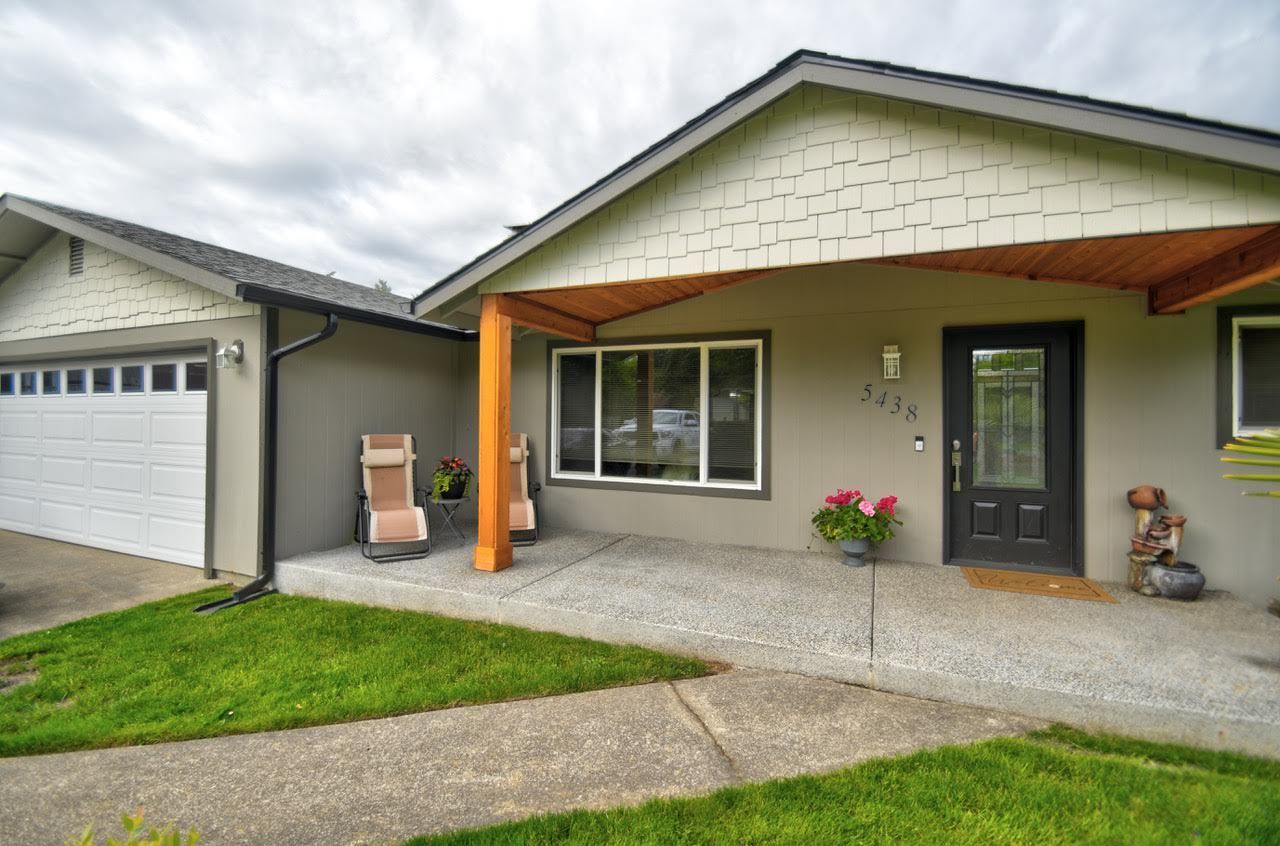 Gray house with attached garage, porch with wooden post, and green lawn.