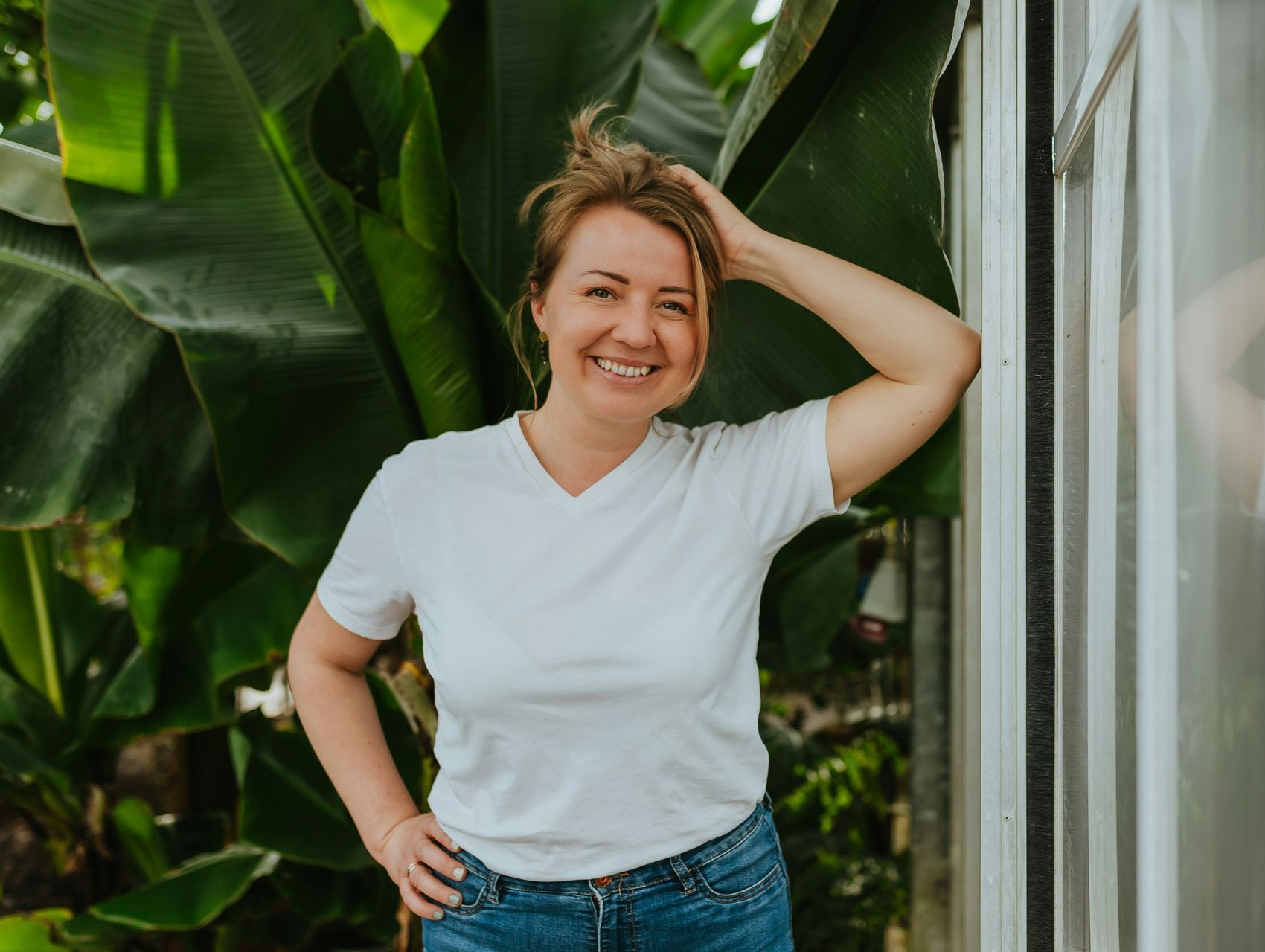 A woman in a white t-shirt and jeans is standing next to a window.