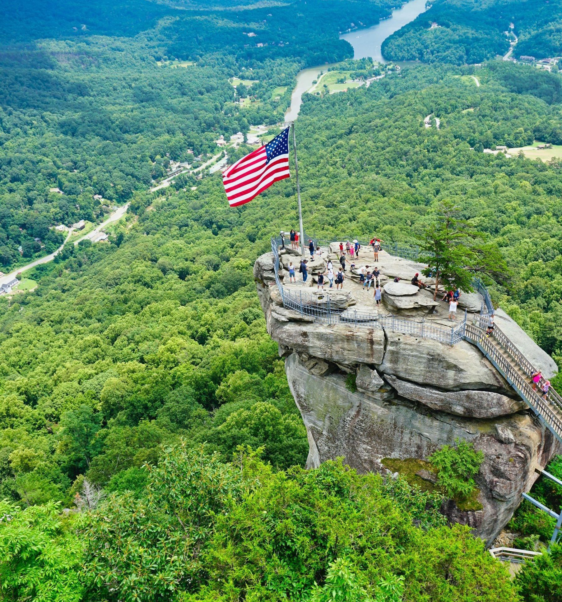 An american flag is flying on top of a rocky cliff overlooking a river.