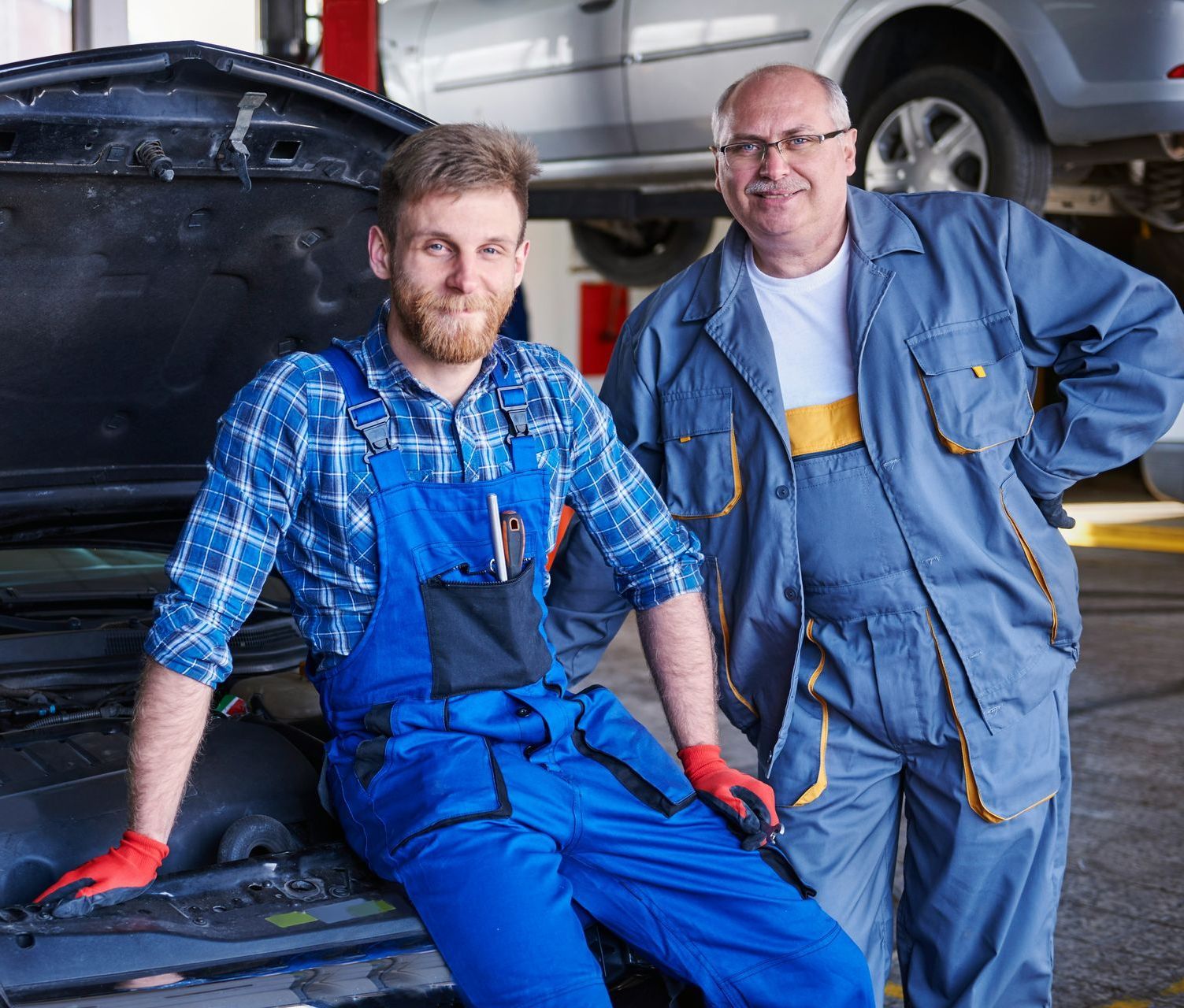 Two men are standing next to each other in front of a car in a garage.