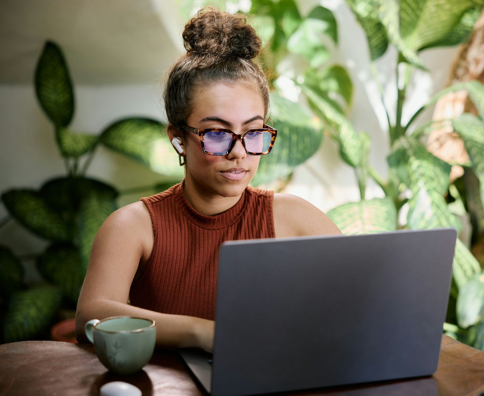 A woman wearing glasses is sitting at a table using a laptop computer.