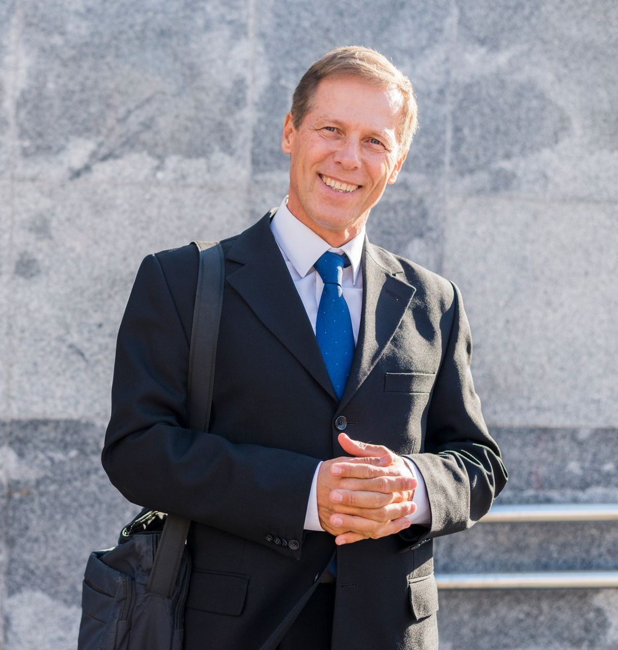 A man in a suit and tie is smiling with his hands folded